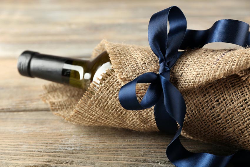 Darčeková fľaša vína zabalená vo vrecovine s ozdobnou mašľou