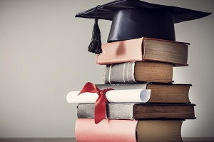 Knihy naskladané jedna na druhej a na vrchnej leží položený absolventský klobúk